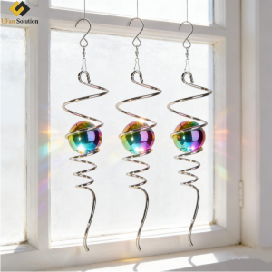 A Spiral Tail Wind Spinner with a colorful gazing ball hanging in front of a frosted window, catching soft light.